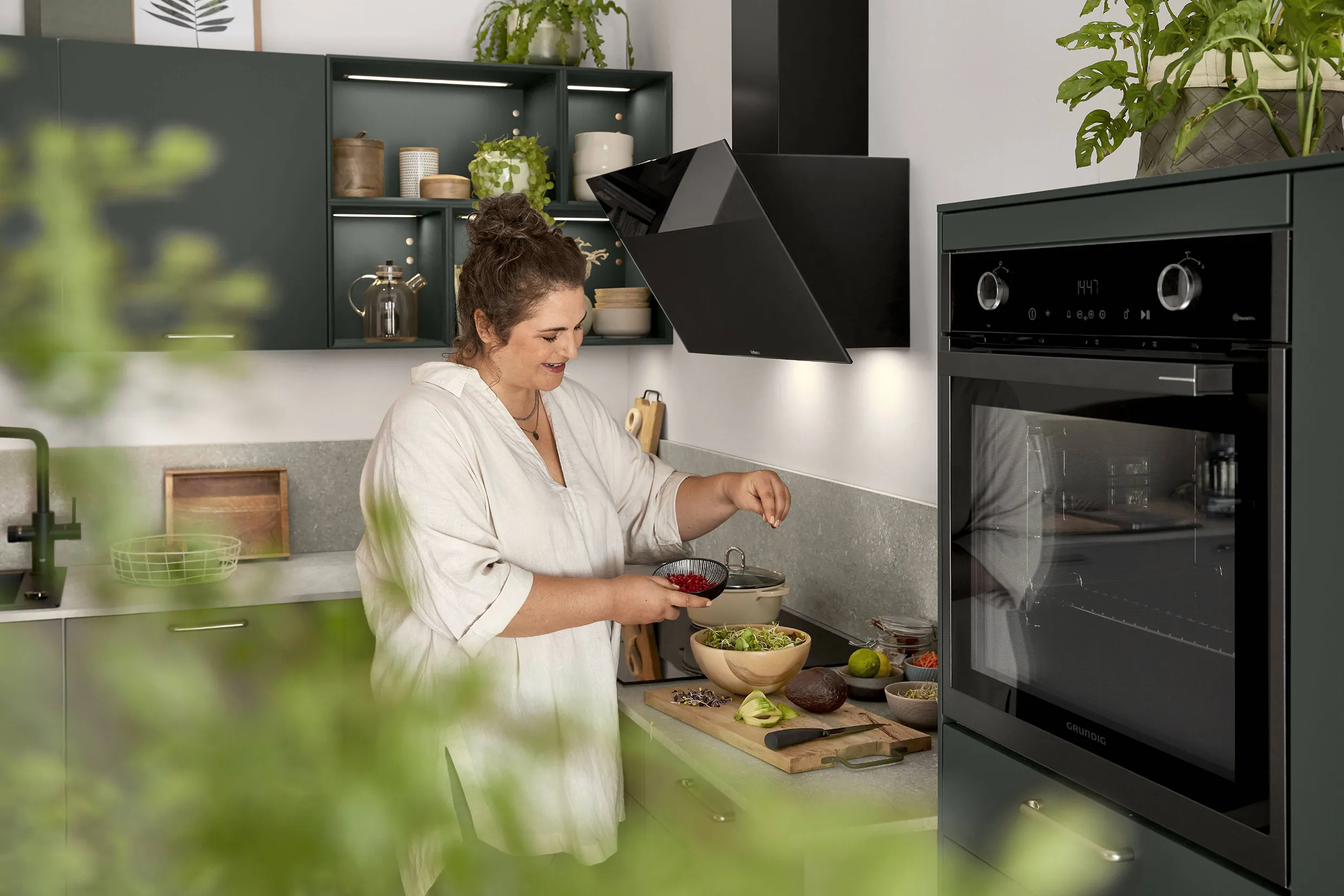 Woman preparing food in a modern kitchen with dark green cabinets and a stylish backsplash, showcasing sleek design and natural accents. Woman preparing food in a modern kitchen with dark green cabinets and a stylish backsplash, showcasing sleek design and natural accents.