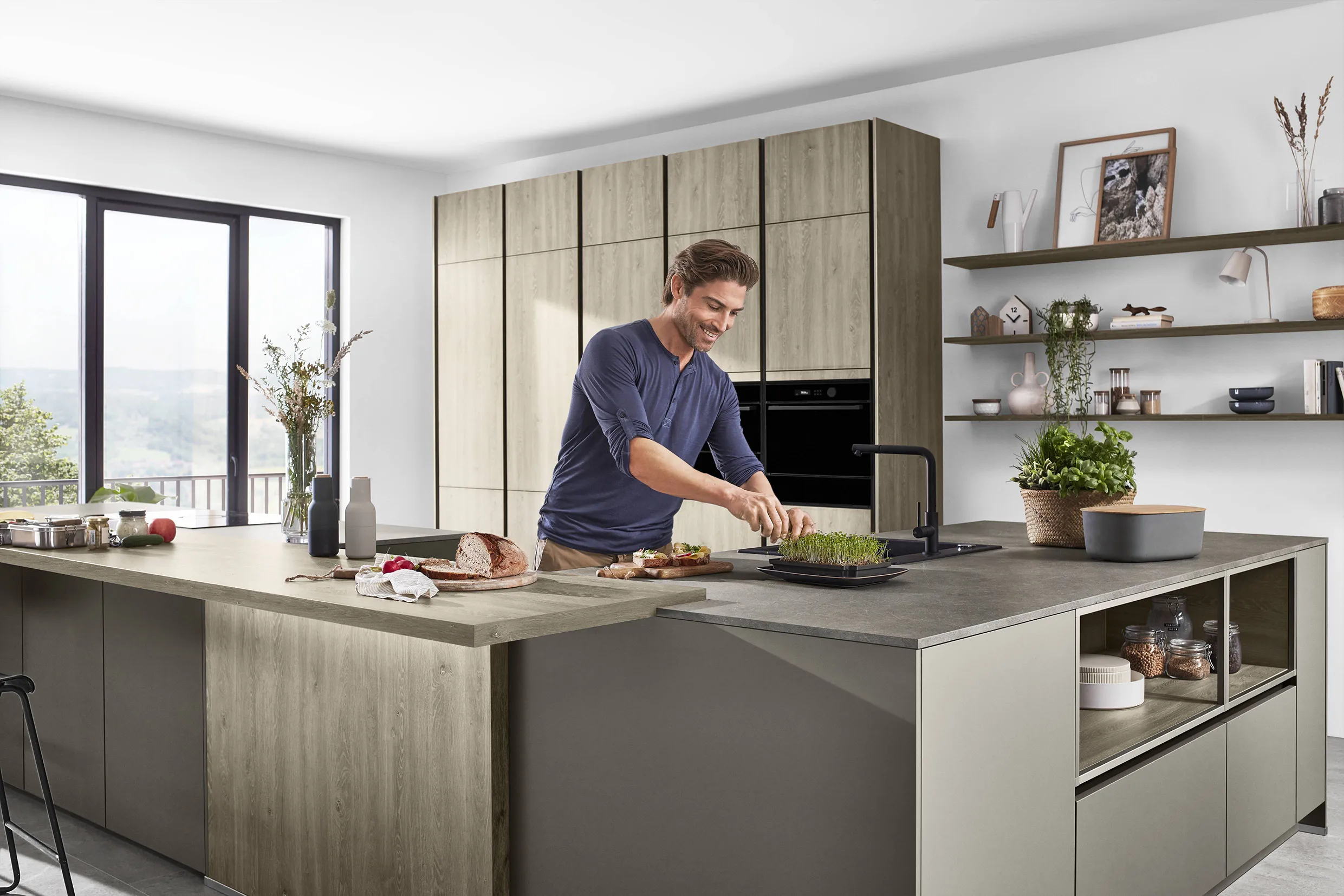 Man preparing food in a modern kitchen with warm wood cabinetry, open shelving, and a spacious two-tone island, capturing a dream kitchen atmosphere. Man preparing food in a modern kitchen with warm wood cabinetry, open shelving, and a spacious two-tone island, capturing a dream kitchen atmosphere.